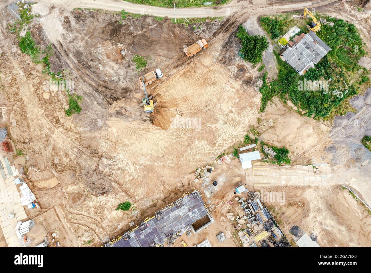 vista aerea dall'alto verso il basso di un escavatore e di autocarri da scarico in cantiere. preparazione del sito per la costruzione di edifici residenziali Foto Stock