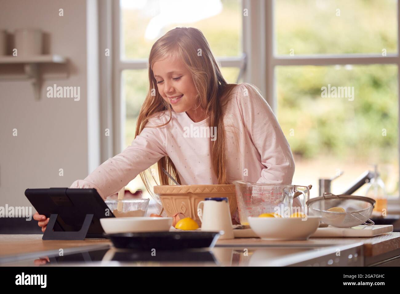 Ragazza che indossa Pajamas fare Pancakes in cucina a casa seguendo la ricetta su Digital Tablet Foto Stock