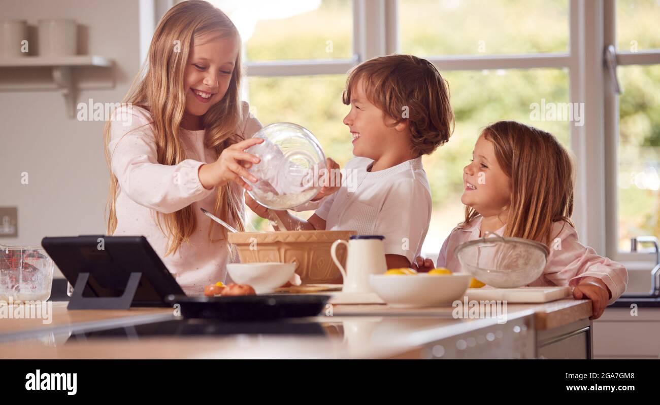 Bambini in Pajamas fare Pancakes in cucina a casa seguendo la ricetta su Digital Tablet Foto Stock
