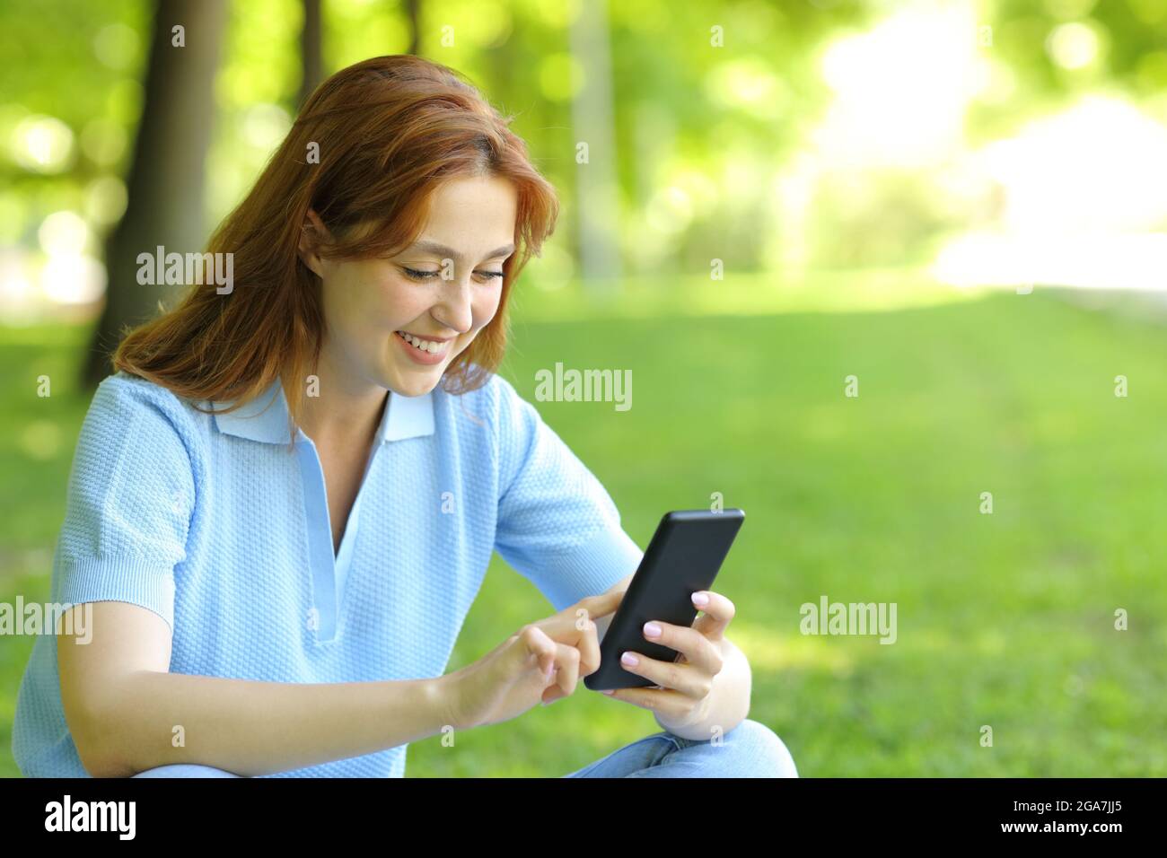 Donna felice che usa un telefono cellulare per controllare i contenuti seduti in un parco Foto Stock