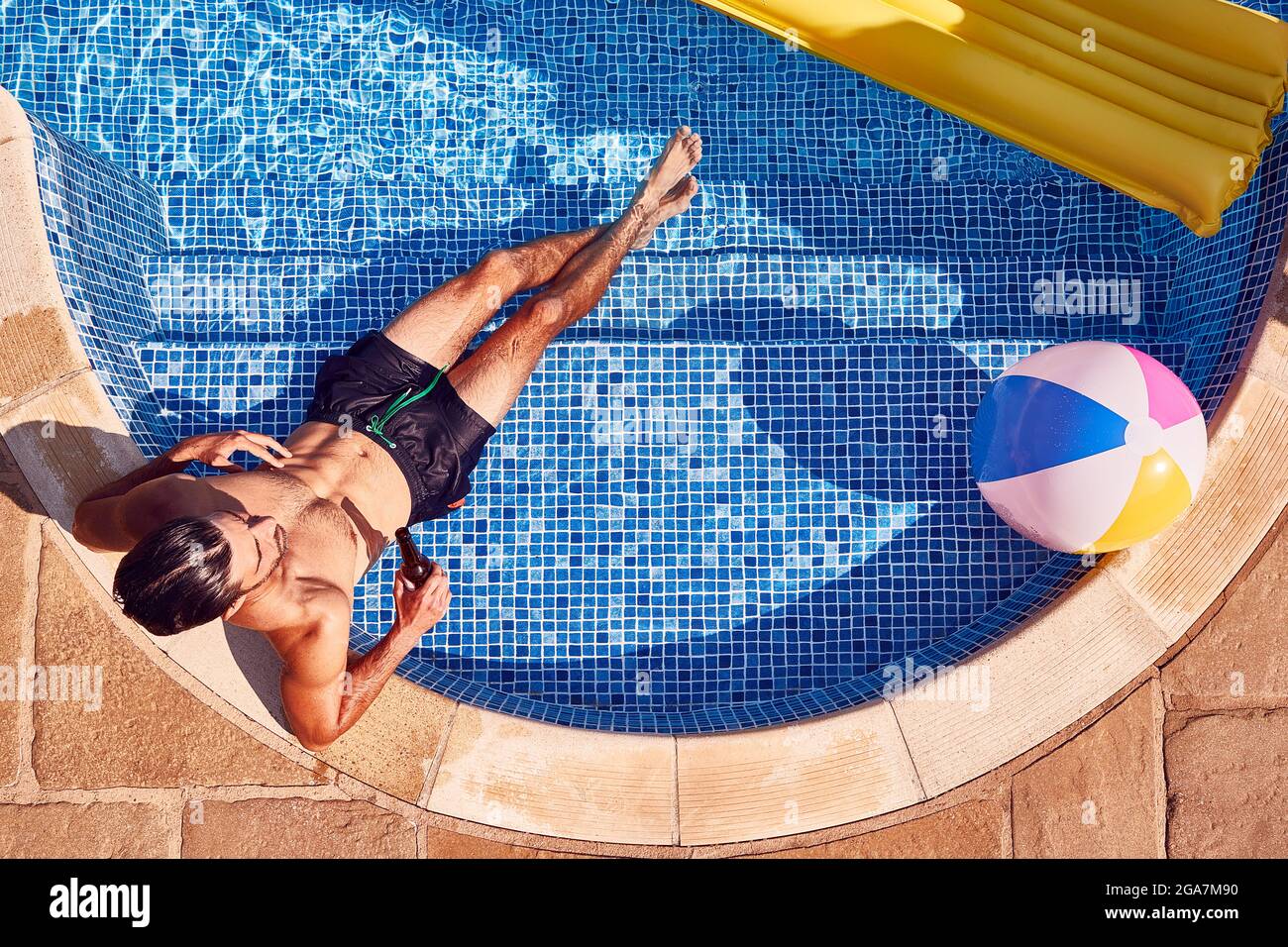 Overhead Tiro di uomo in Shorts da bagno relax in piscina all'aperto bere birra Foto Stock