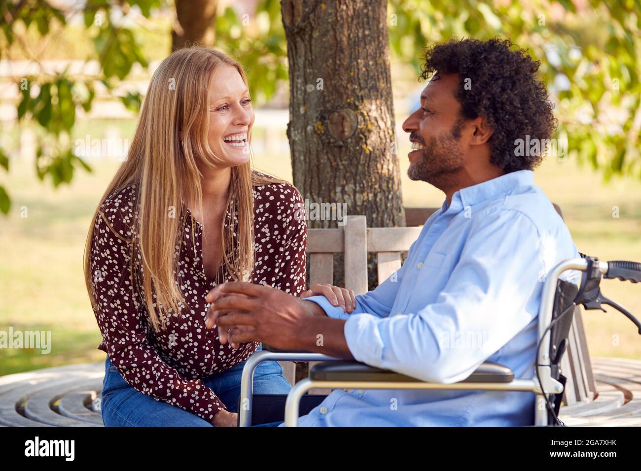 Coppia matura con uomo seduto in sedia a rotelle che parla a Park insieme Foto Stock