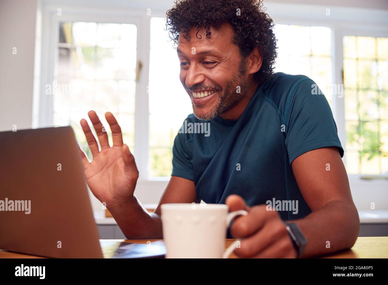 Uomo maturo a casa in cucina sventolando come fa la videochiamata sul computer portatile Foto Stock