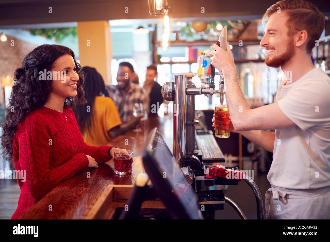 Sorridente barista maschio dietro bancone servire cliente femminile con birra Foto Stock