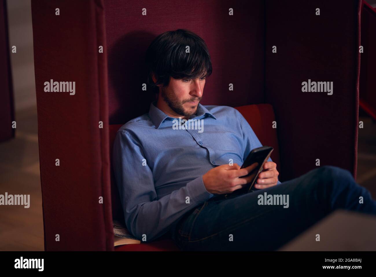 Uomo d'affari nell'area della lobby dell'ufficio moderno a piano aperto che verifica i messaggi sul telefono cellulare Foto Stock
