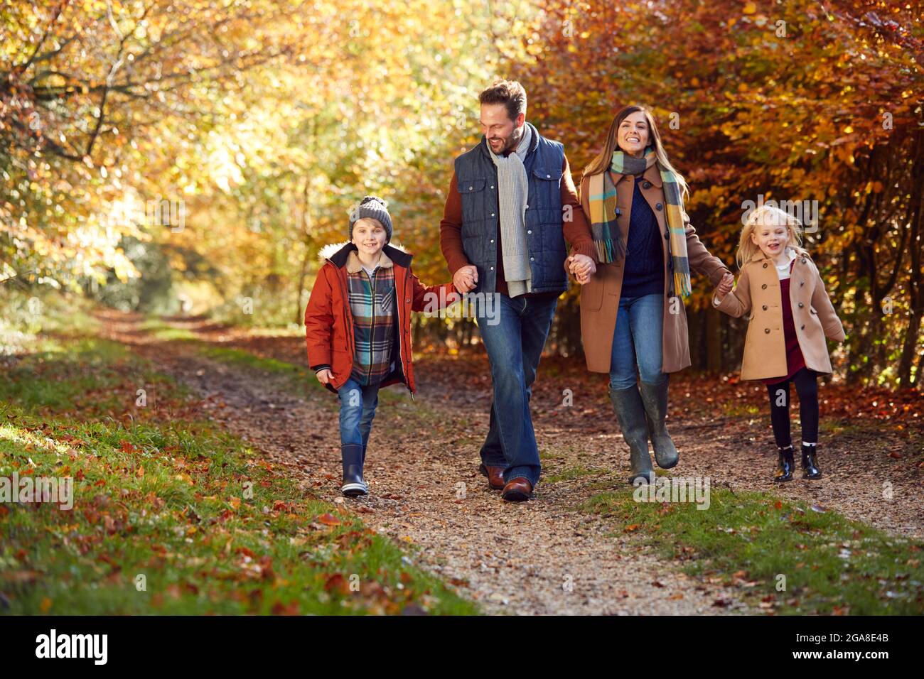 Famiglia con genitori maturi e due bambini che tiene le mani camminando lungo la pista nella campagna autunnale Foto Stock