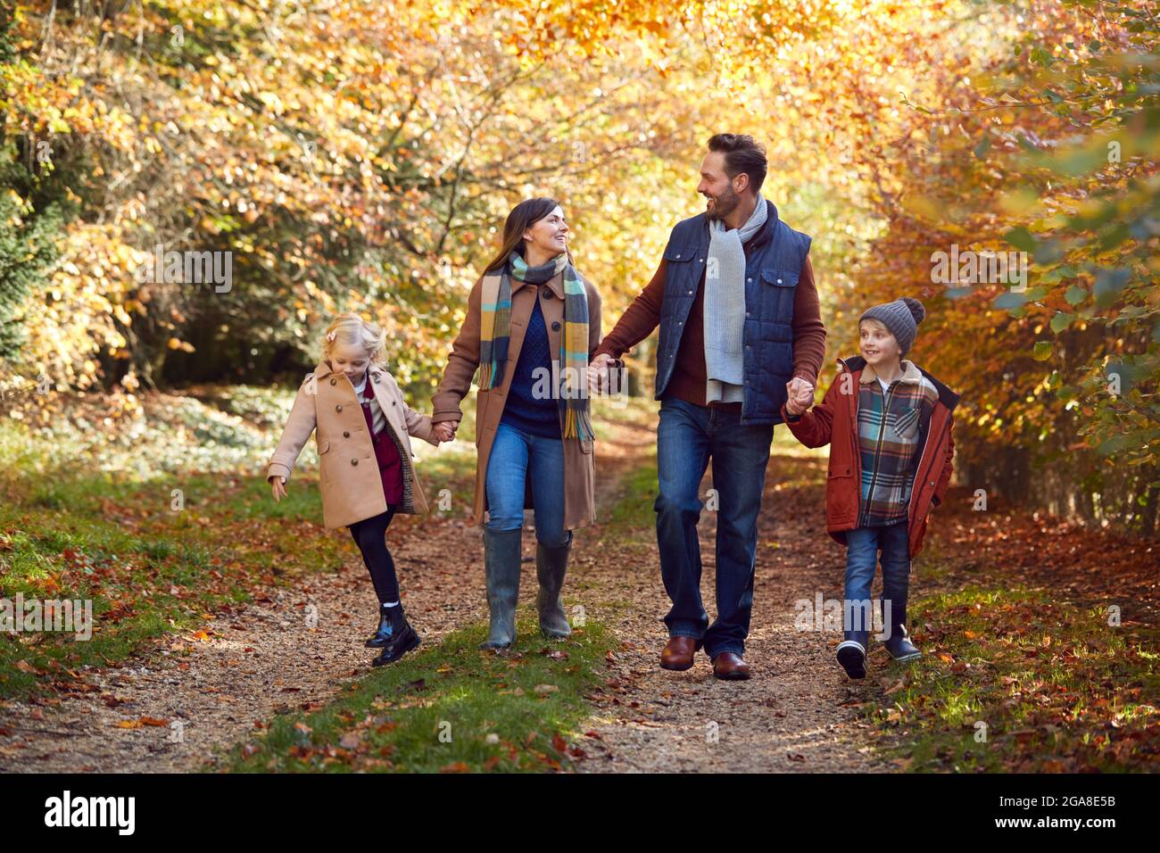 Famiglia con genitori maturi e due bambini che tiene le mani camminando lungo la pista nella campagna autunnale Foto Stock