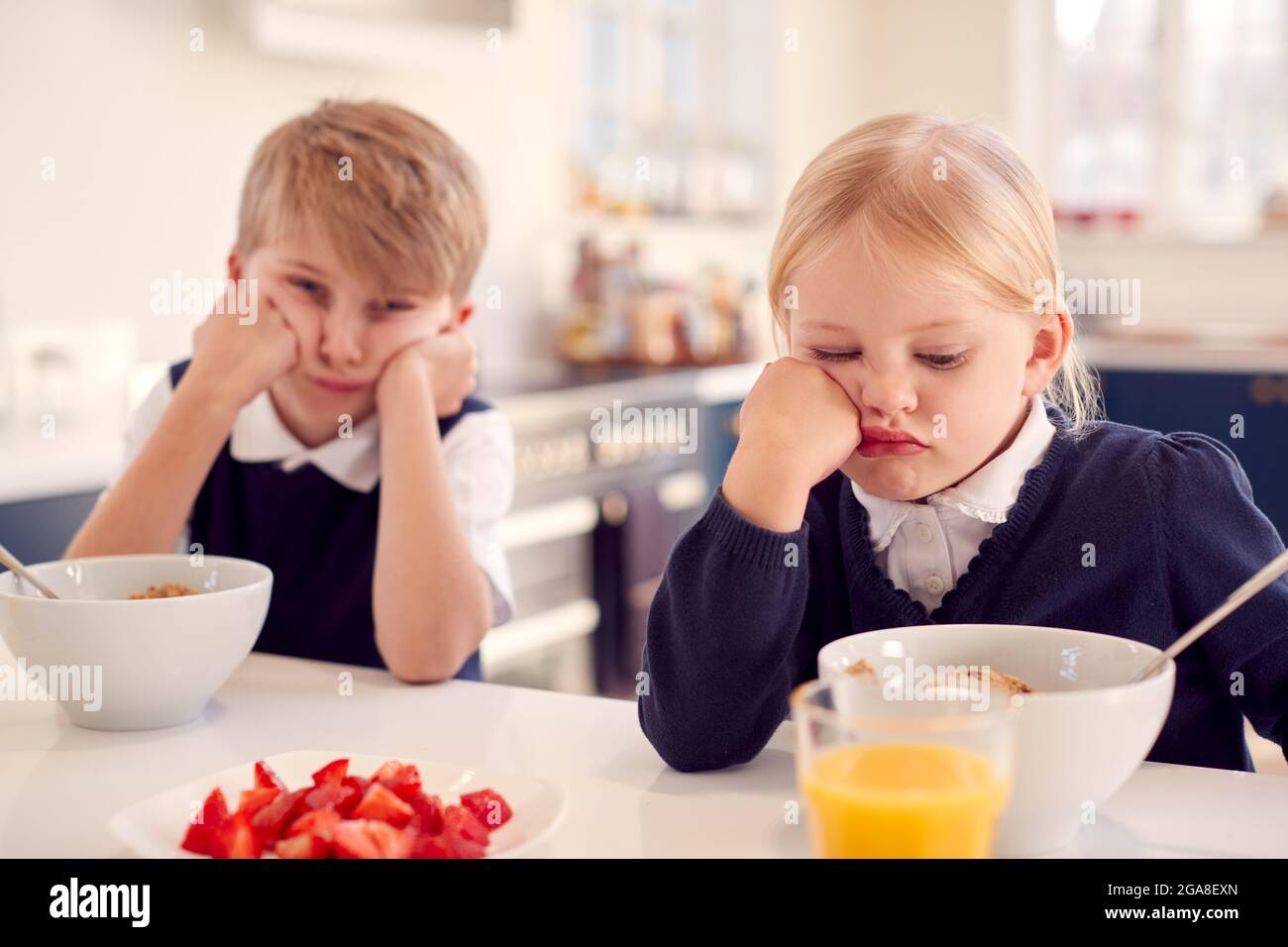 Ritratto di due bambini che indossano l'uniforme della scuola in cucina che mangiano la colazione Foto Stock