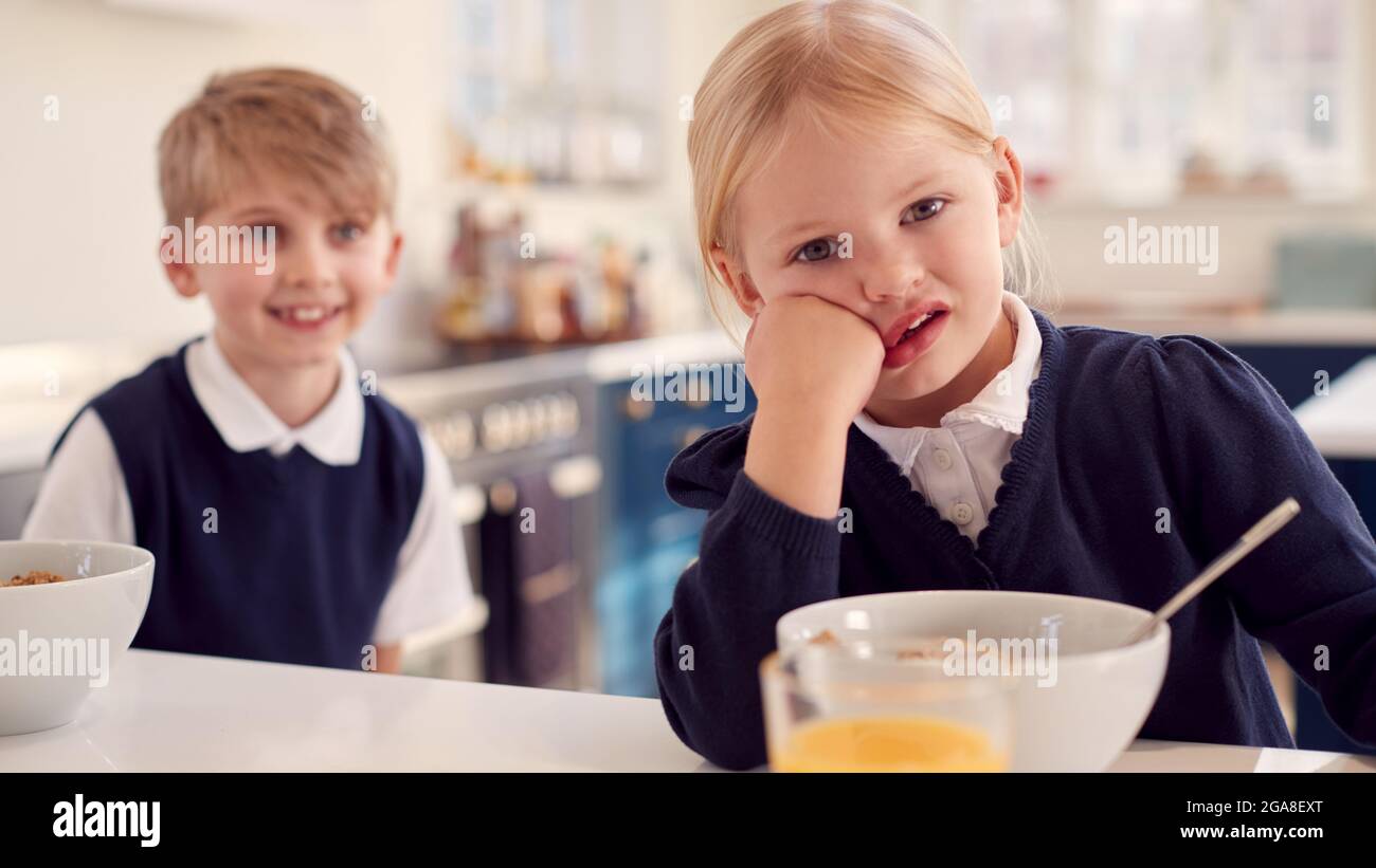 Ritratto di due bambini che indossano l'uniforme della scuola in cucina che mangiano la colazione Foto Stock