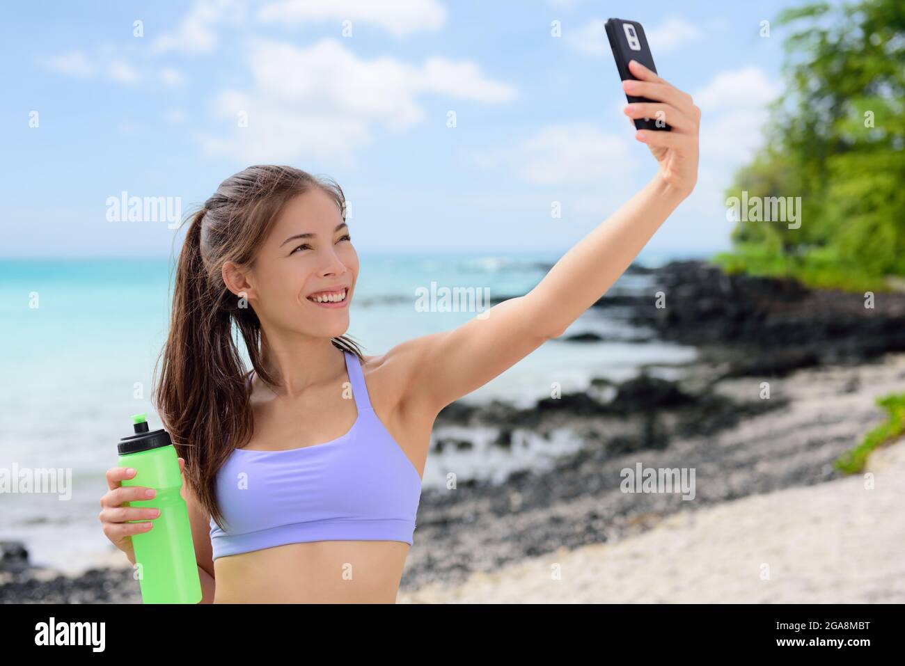 Donna sorridente e sportiva che prende Selfie sulla spiaggia Foto Stock