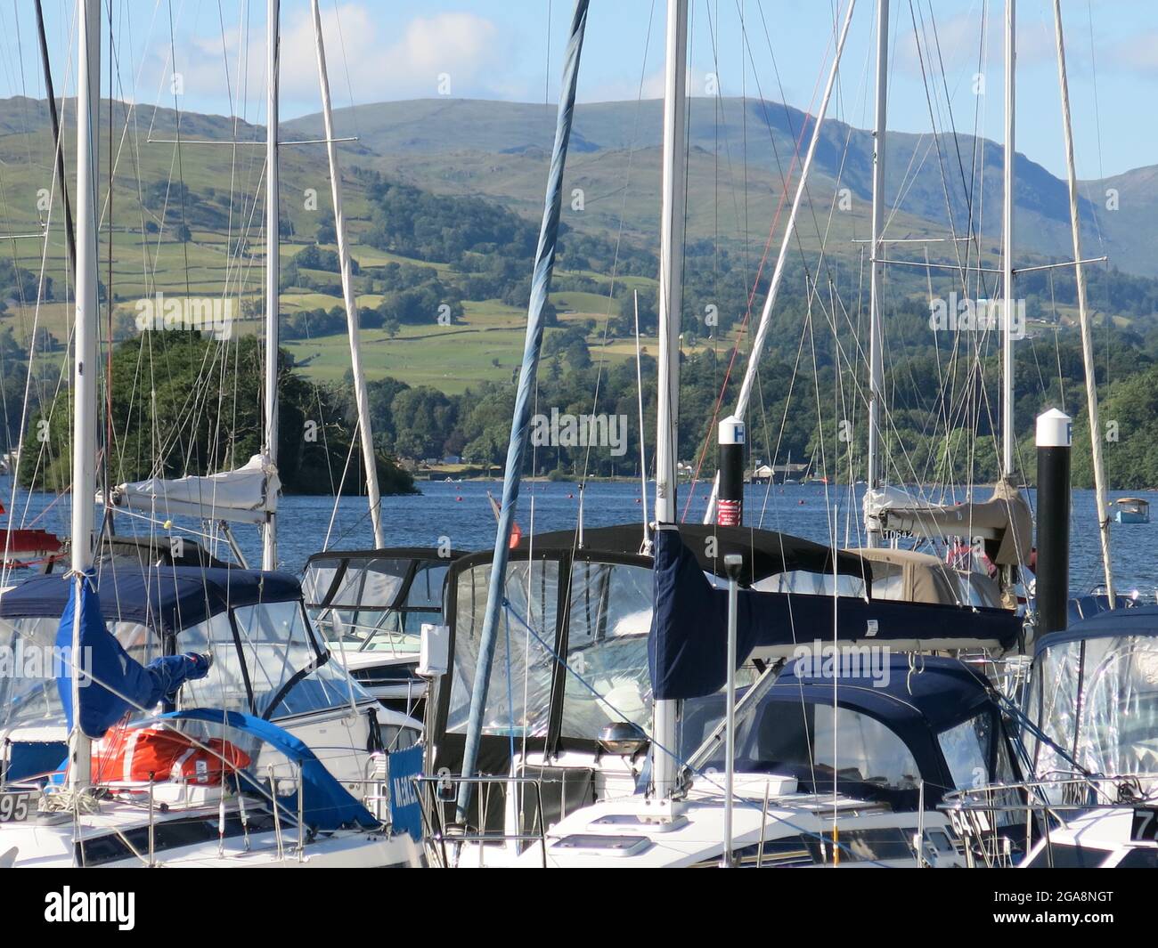 Il panorama mozzafiato delle montagne e del lago Windermere si intravede attraverso le alte cime delle barche a vela e degli yacht ormeggiati nel porticciolo di Bowness. Foto Stock
