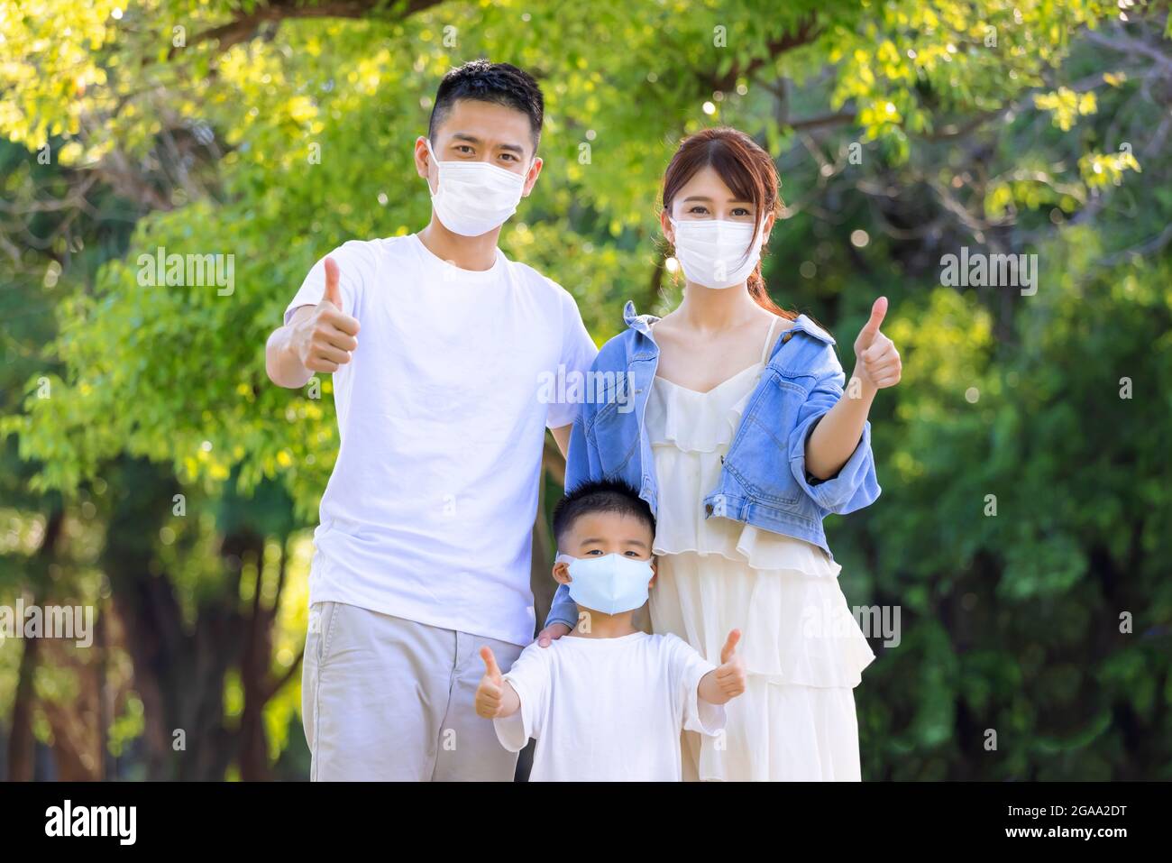 Famiglia felice indossare maschere mediche a protezione e mostrare pollici in su Foto Stock