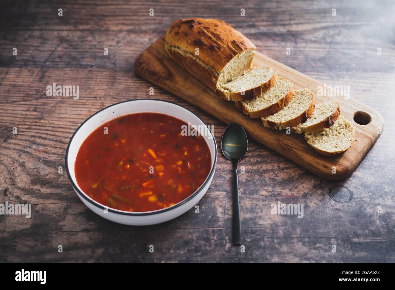 zuppa vegana di pomodoro e verdure con pane fatto in casa con latte di soia ed erbe su tagliere di legno su fondo rustico di legno, sano pianta-b Foto Stock