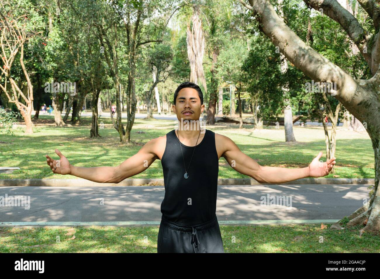 Giovane brasiliano, insegnante di yoga, a braccia aperte in un parco pubblico in una giornata di sole. Foto Stock