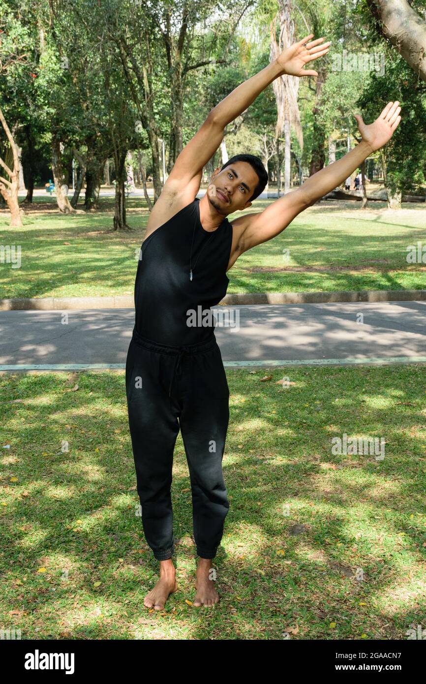 Giovane brasiliano, insegnante di yoga, facendo stretching in un parco pubblico in una giornata di sole. Foto Stock