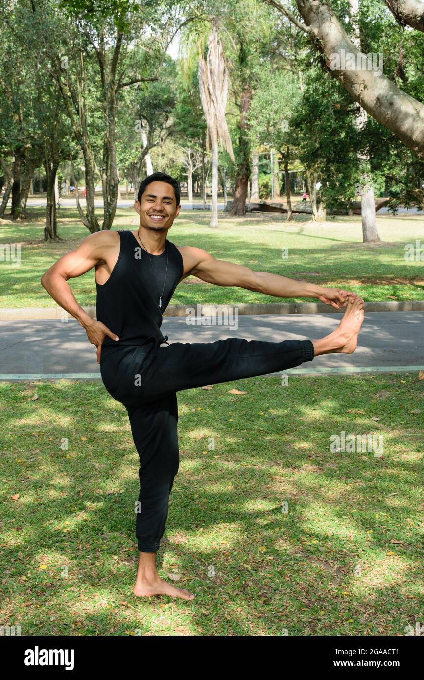 Sorridente giovane brasiliano, in posizione equilibrata, in un parco pubblico in una giornata di sole. Foto Stock