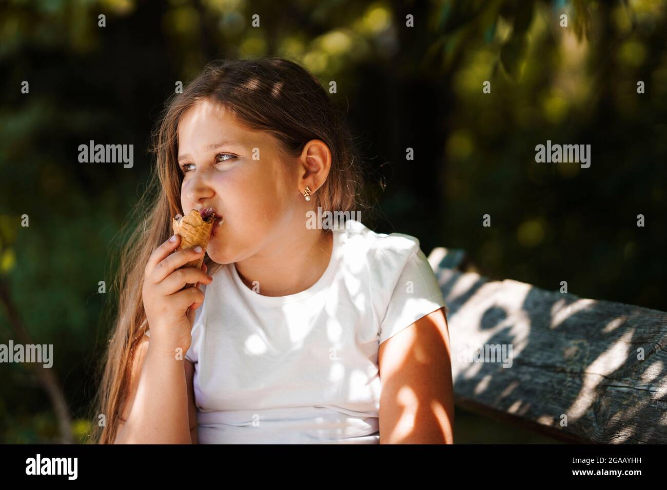Ragazza caucasica seduta sulla panchina e mangiare gelato . Ragazzino sorridente e sognante. Ora legale. Foto Stock