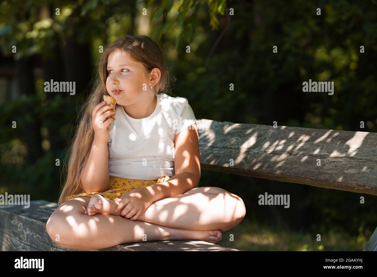Ragazza caucasica seduta sulla panchina e mangiare gelato . Ragazzino sorridente e sognante. Ora legale. Felice infanzia. Foto Stock