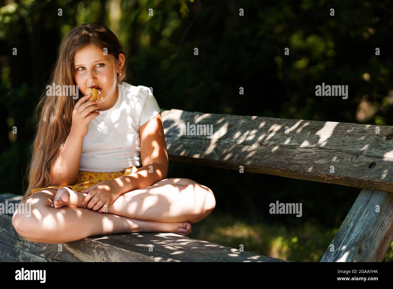 Carino ragazza caucasica divertente seduta sulla panchina e mangiare gelato . Ragazzino sorridente e sognante. Ora legale. Felice infanzia. Foto Stock