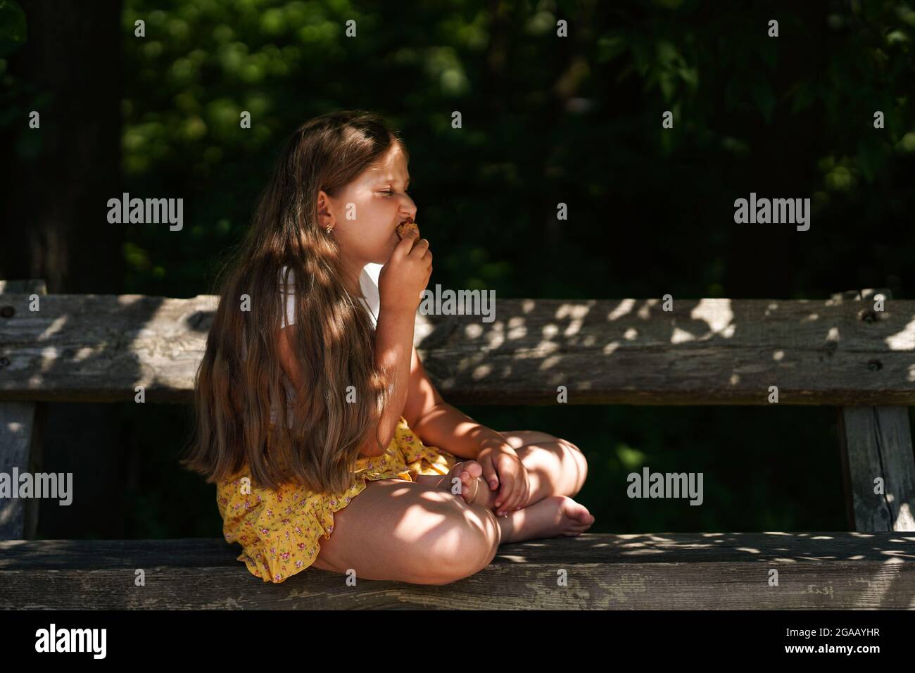 Carino ragazza caucasica divertente seduta sulla panchina e mangiare gelato . Ragazzino sorridente e sognante. Ora legale. Felice infanzia. Foto Stock