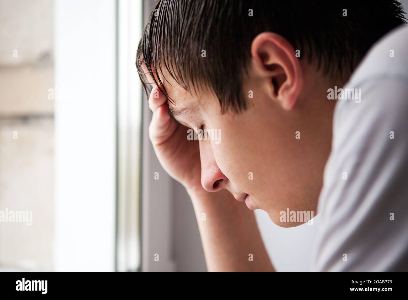 Uomo giovane triste vicino alla finestra nella stanza Foto Stock
