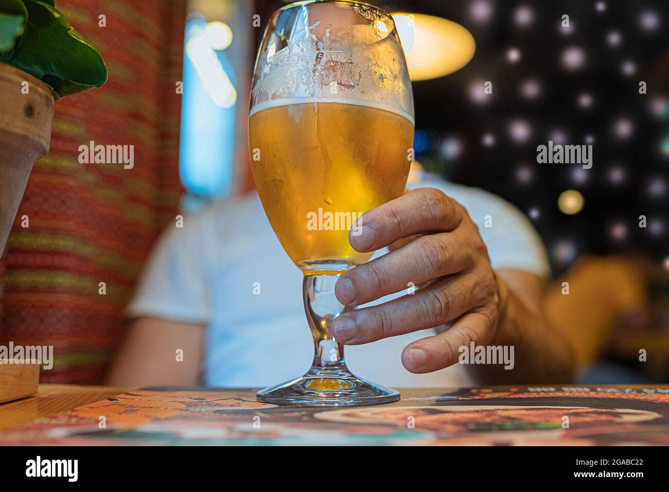 La mano dell'uomo abbassa il bicchiere e versa la birra su sfondo sfocato. Foto Stock