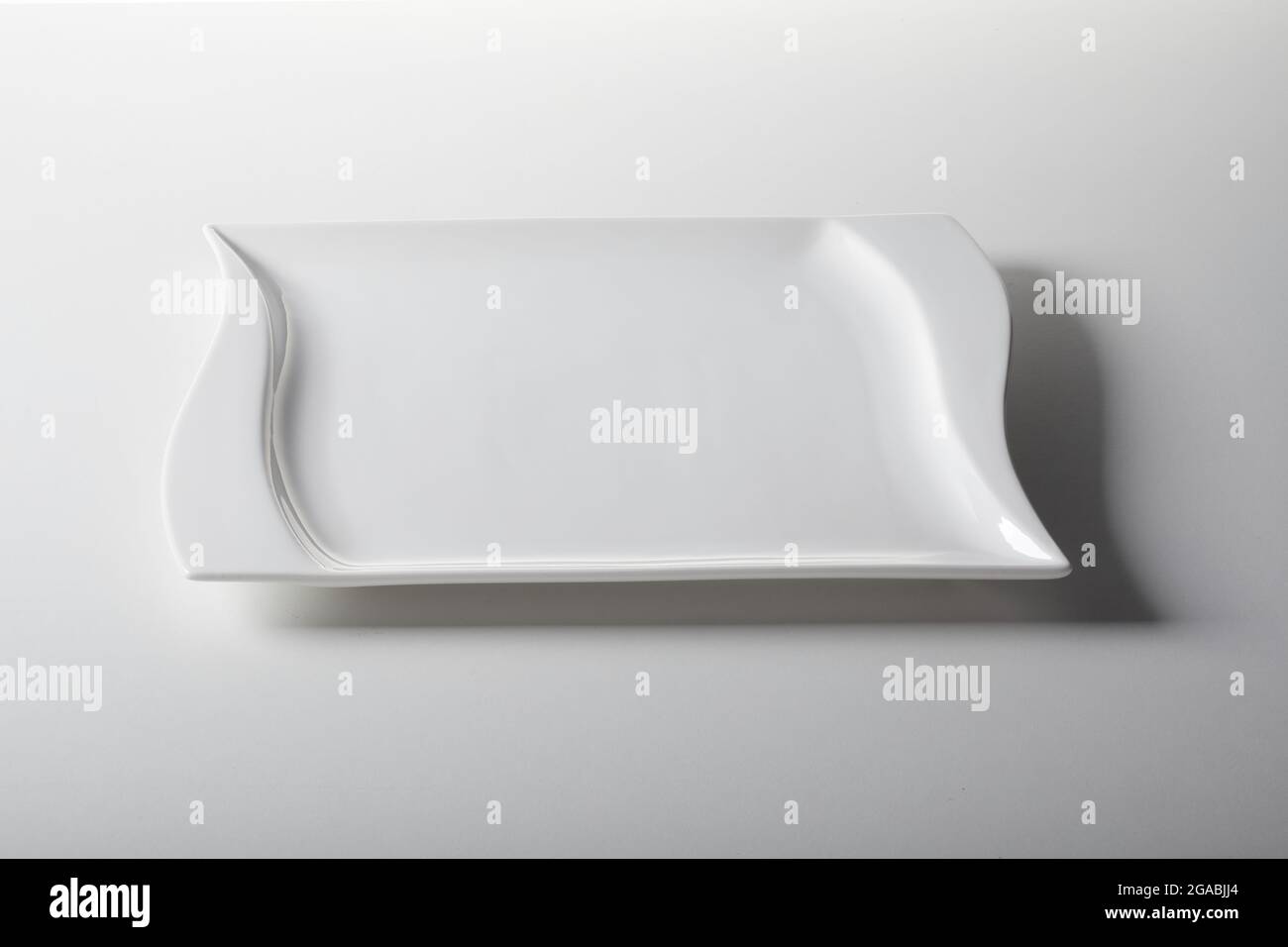 Alto angolo di piatto ondulato vuoto in ceramica posto su sfondo bianco in cucina Foto Stock