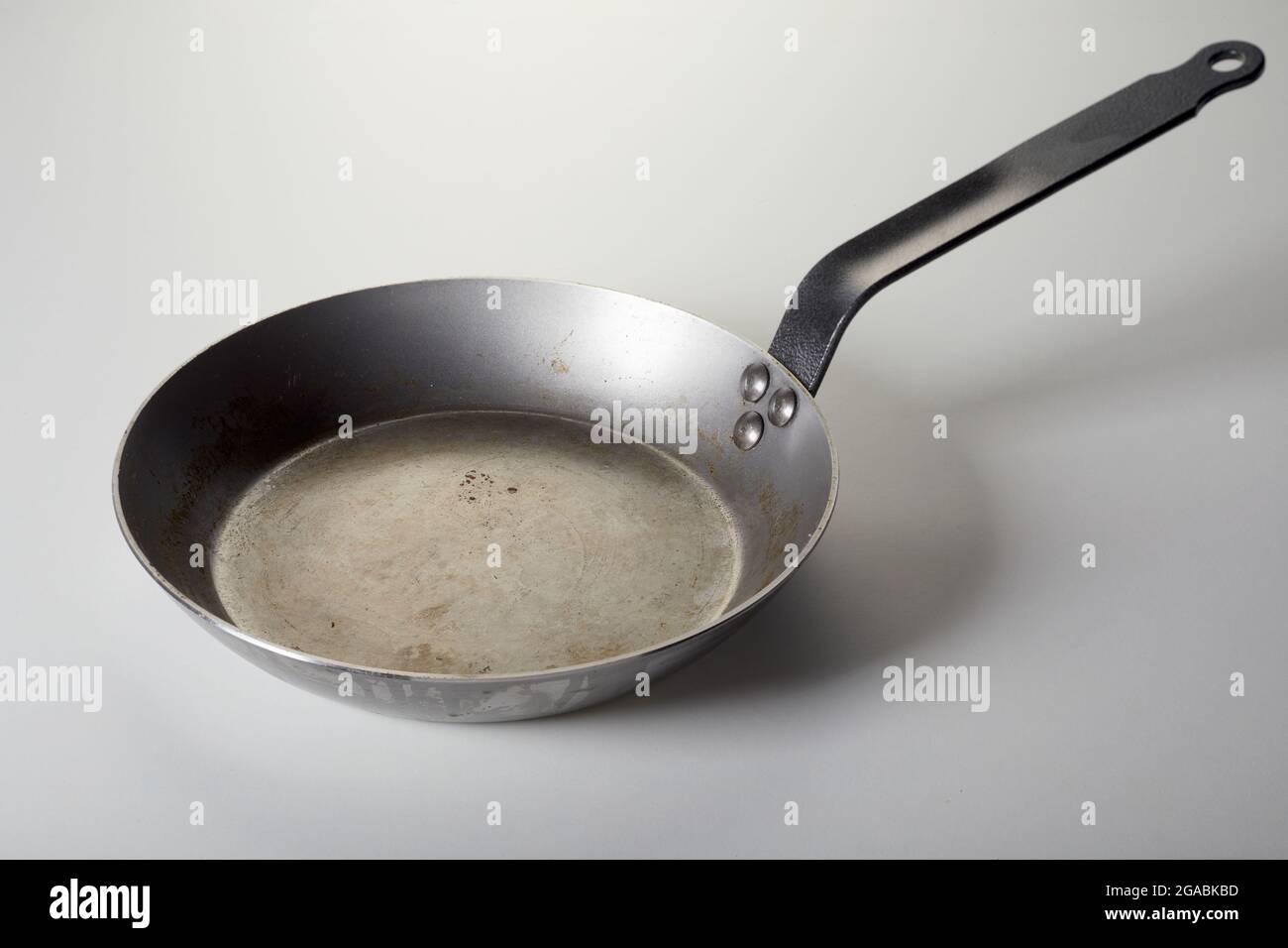 Angolo alto di vecchia padella in metallo lucido posta sul tavolo bianco in cucina Foto Stock