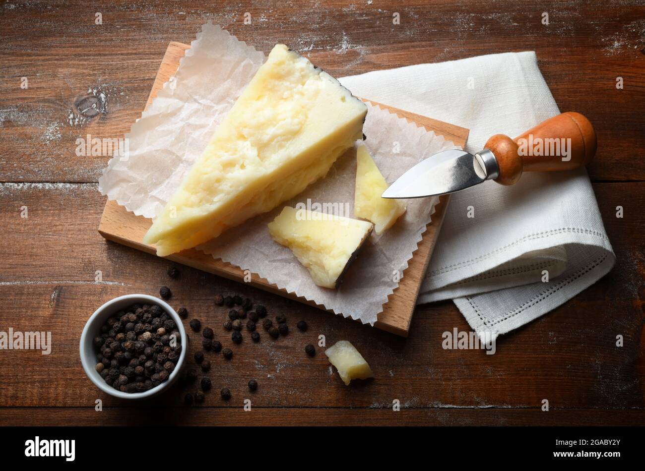 Pezzi di pecorino su tagliere con tovagliolo bianco, coltello per formaggi stagionati e pepe nero. Rustico sfondo in legno, vista ad alto angolo. Foto Stock