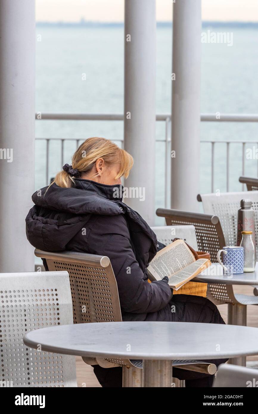 giovane femmina seduta all'aperto lettura di un libro, signora seduta al caffè lettura di un libro, giovane donna lettura di un libro fuori porta, lettore con libro avvincito Foto Stock