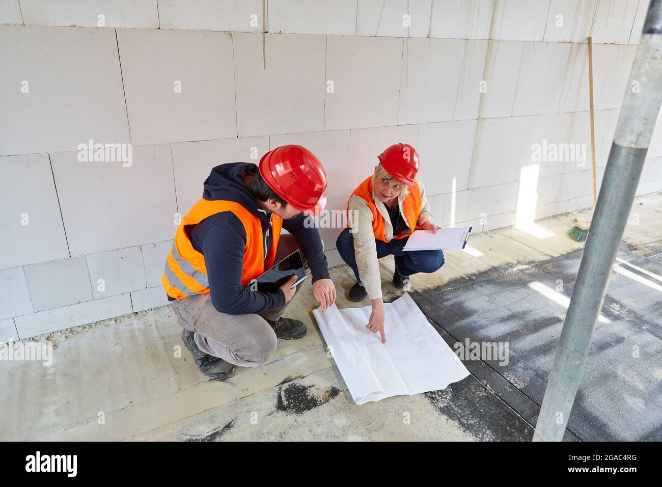 Architetto e artigiano con disegno di costruzione discutono di progetto di costruzione nella conchiglia del cantiere Foto Stock