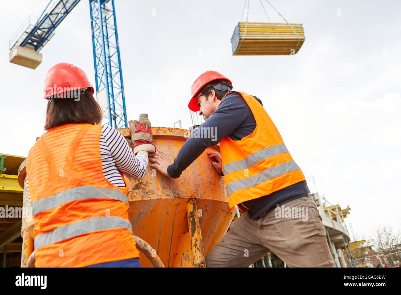 I lavoratori edili lavorano insieme su betoniera con legname su gru da cantiere sullo sfondo Foto Stock