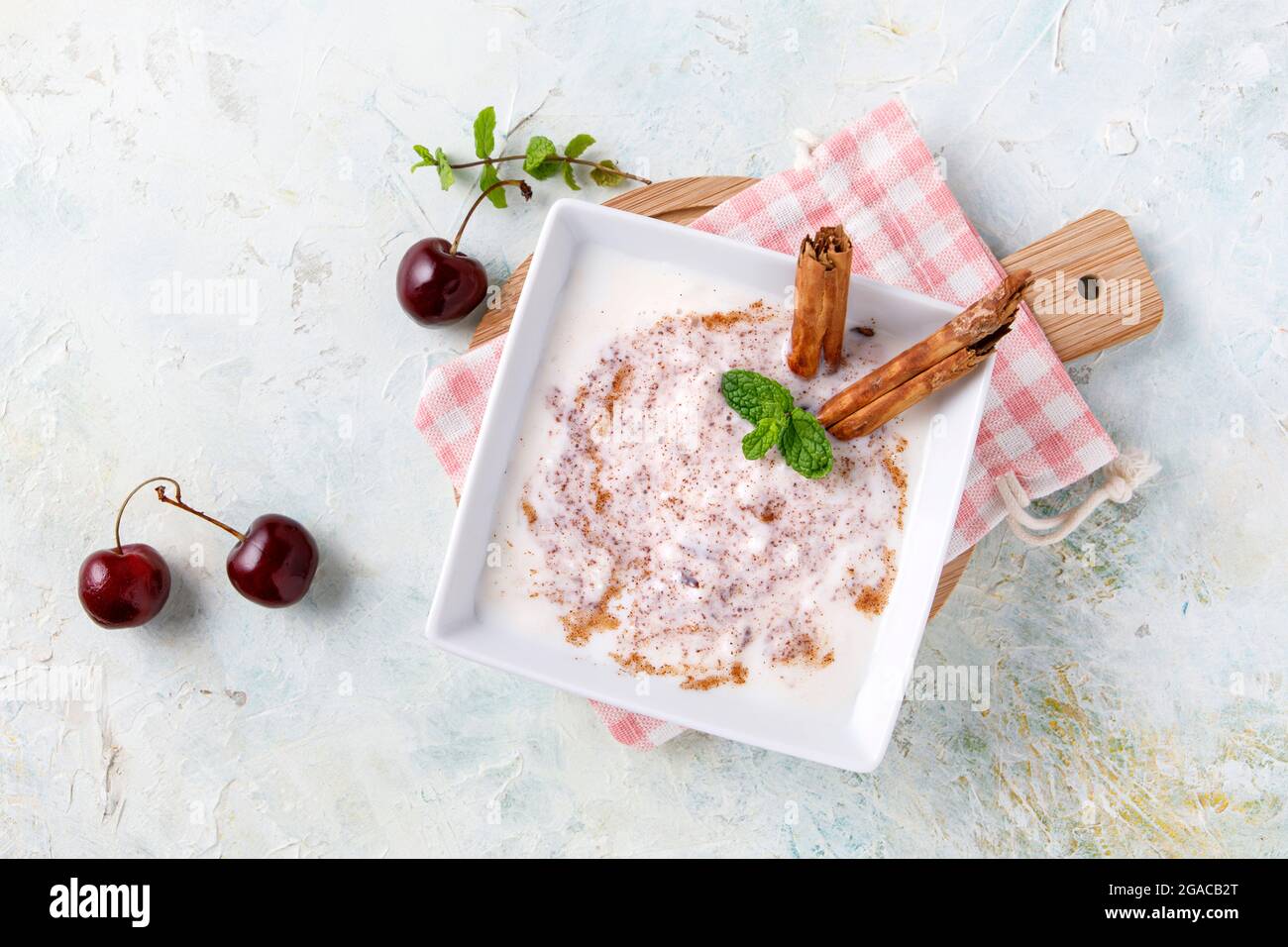 Budino di riso fatto in casa con cannella e ciliegie in una ciotola bianca su legno Foto Stock