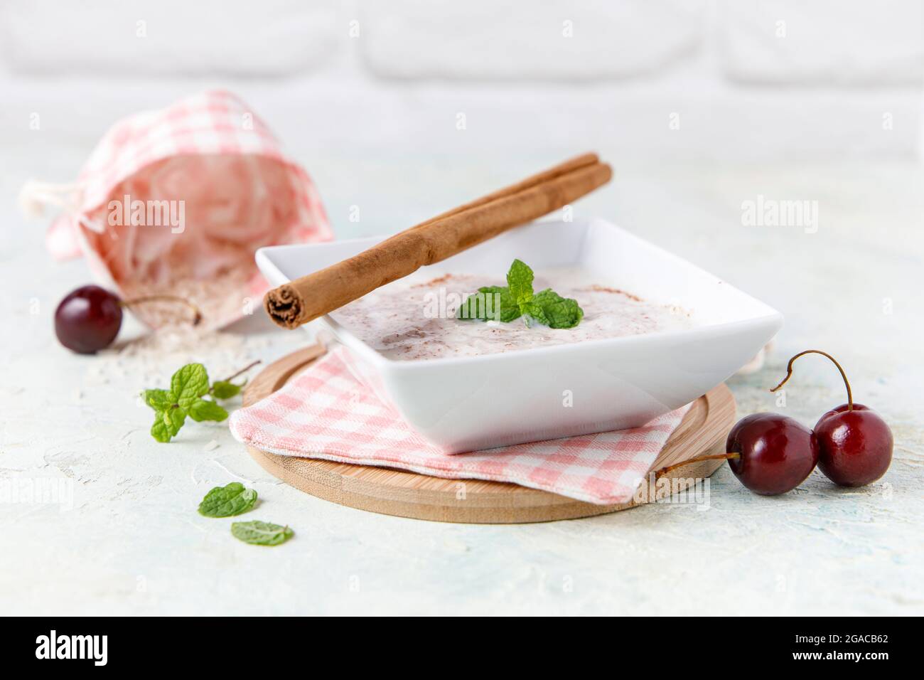Budino di riso fatto in casa con cannella e ciliegie in una ciotola bianca su legno Foto Stock