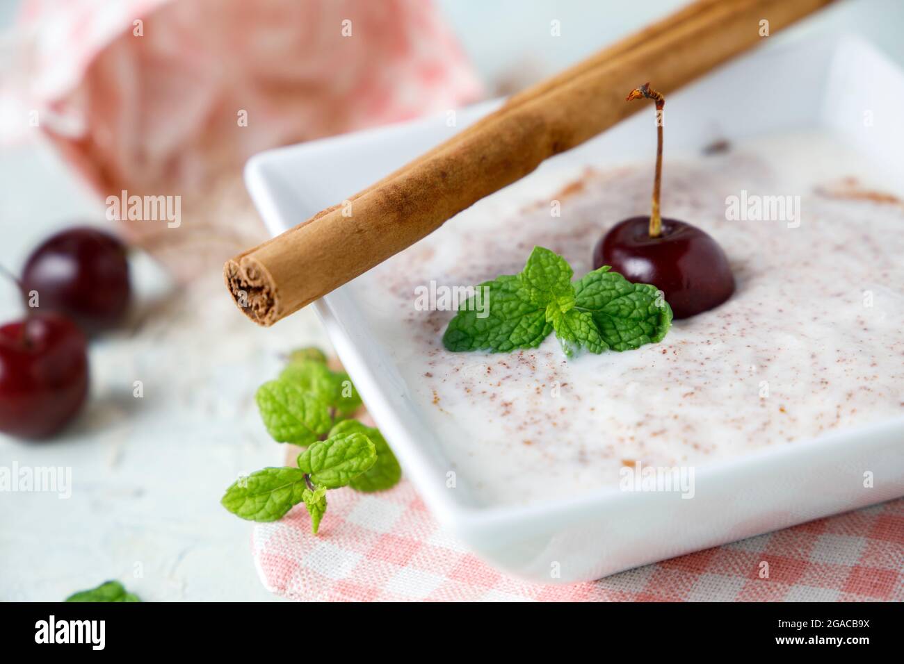 Budino di riso fatto in casa con cannella e ciliegie in una ciotola bianca su legno Foto Stock