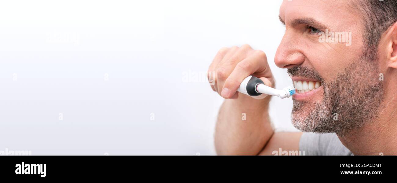 L'uomo pulisce i denti con uno spazzolino elettrico. Sbiancamento dei denti, cura dentale Foto Stock