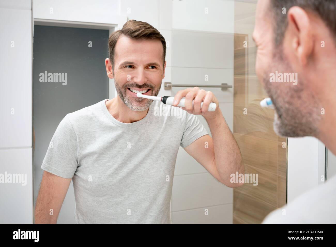 Uomo che gli spazzolava i denti in bagno. Denti bianchi e un bel sorriso, concetto di igiene del mattino Foto Stock
