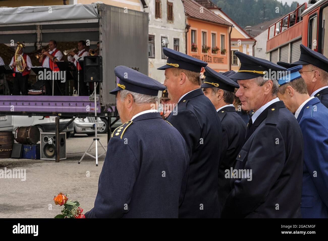 Volontari vigili del fuoco in uniforme blu con cappelli a picco, riuniti  per una cerimonia civica, godersi la musica di Jihočeští Rodáci (nativi  della Boemia meridionale), una band di ottone che suona