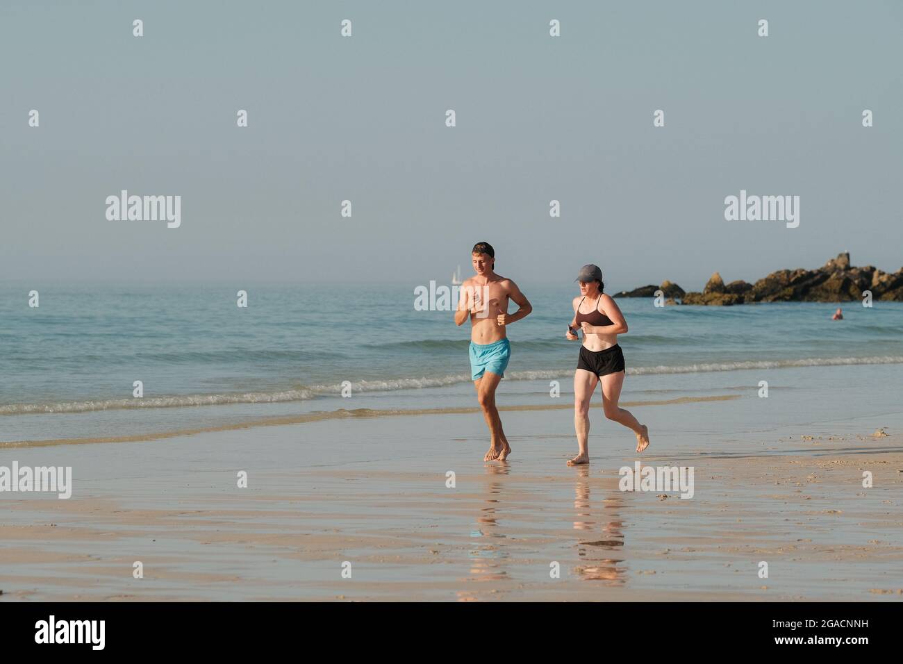 Giovane coppia che corre lungo la spiaggia di Porthmeor a St Ives in Cornovaglia. Foto Stock