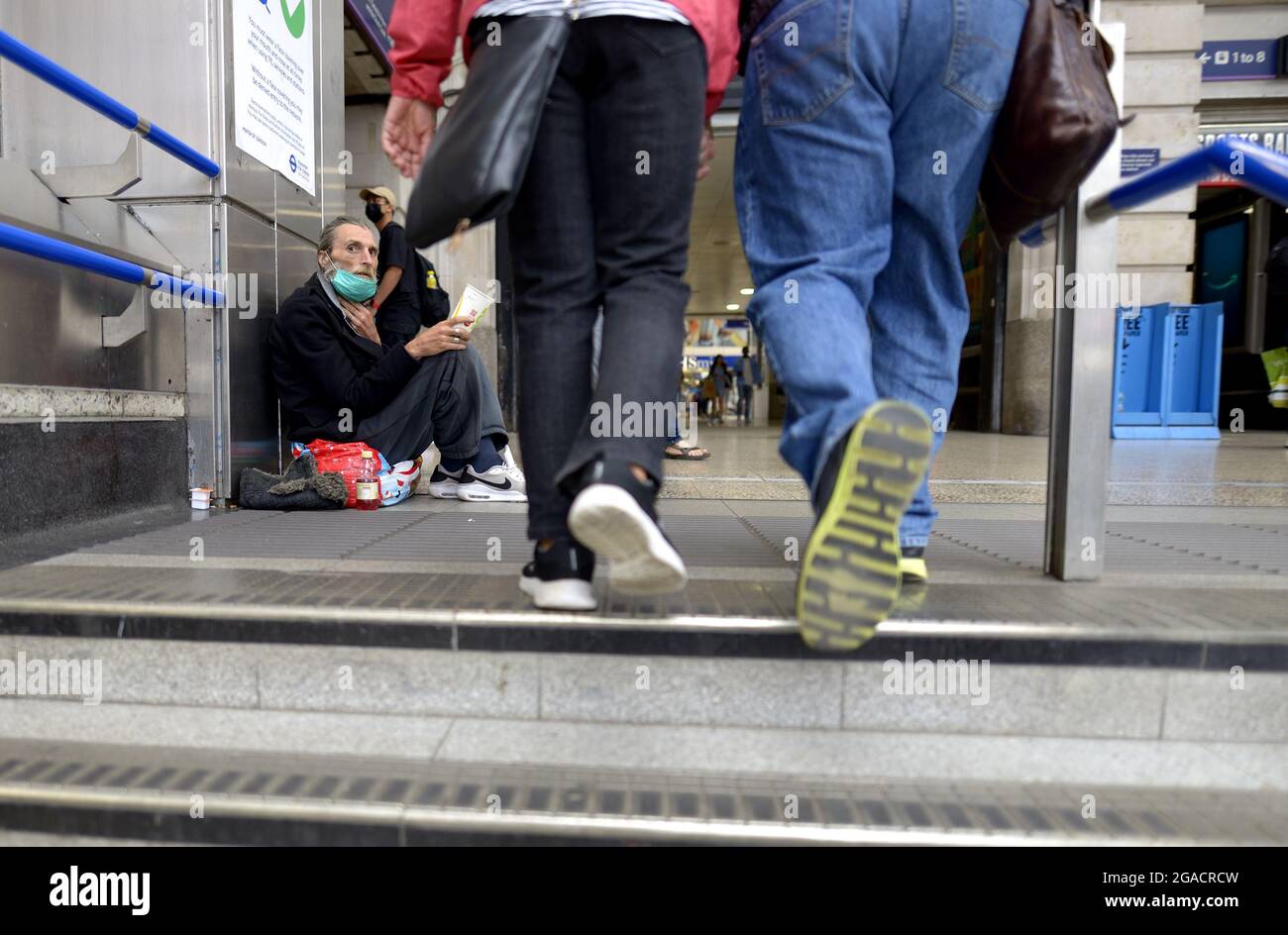 Londra, Inghilterra, Regno Unito. Victoria Station: Uomo senza casa in una maschera COVID viso, che si chiede sui passi in su dalla stazione della metropolitana Foto Stock