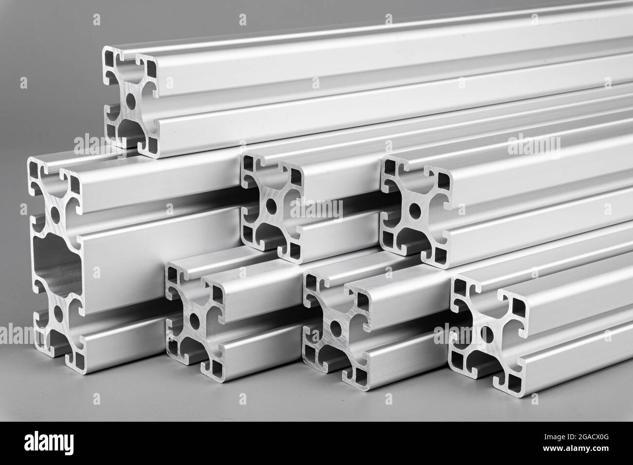 Barre di profilo estrusivo in alluminio su sfondo grigio. Progettazione e progettazione di materiali per l'industria delle costruzioni metalliche. Foto Stock