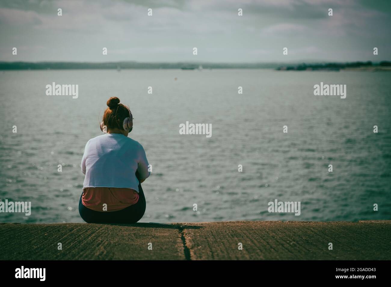Una ragazza adolescente che indossa le cuffie seduto da sola vicino al mare Foto Stock