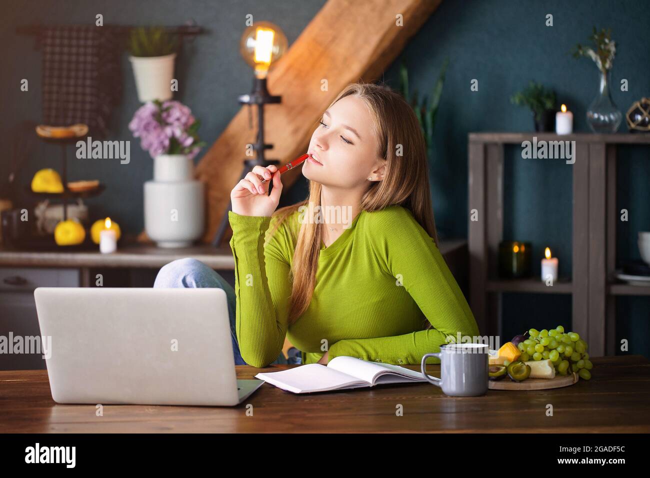 Giovane donna pensiva freelance seduto a casa con il laptop, prendere appunti, guardare attentamente in aria, pensare a nuove idee, blo femminile Foto Stock