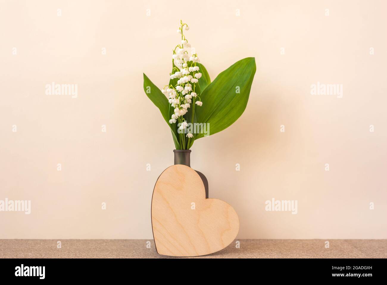 Piccolo bouquet di gigli della valle in bottiglia e cuore in legno vuoto con spazio per il design su sfondo beige Foto Stock