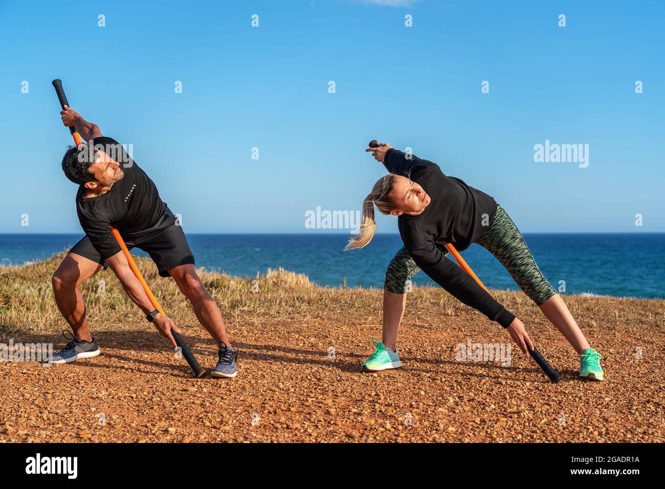 Un uomo e una donna di mezza età sull'oceano stanno facendo un riscaldamento. Lezioni di fitness. Utilizzo di bastoncini da ginnastica per l'allungamento. Foto Stock