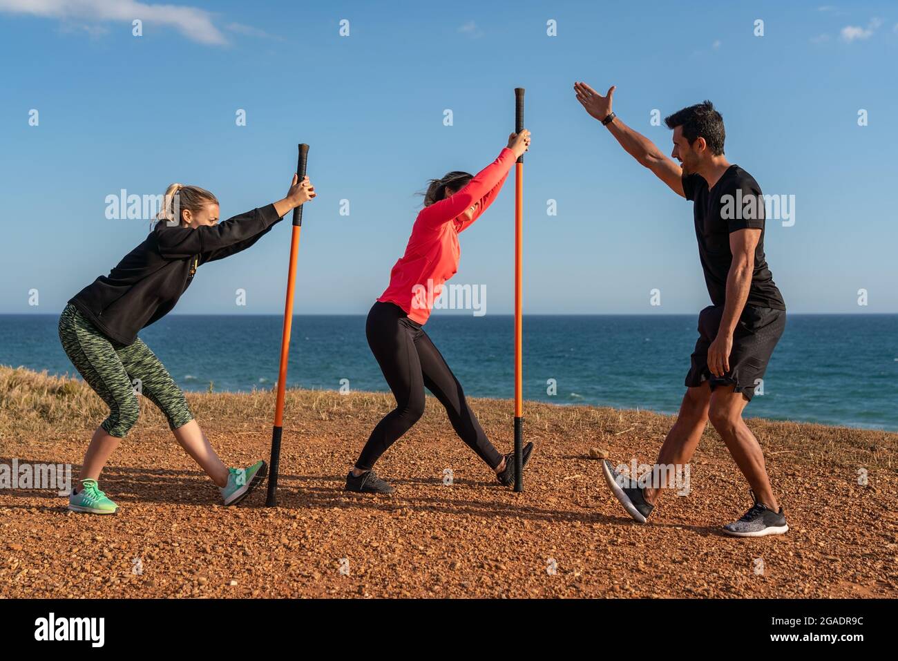 Un uomo e una donna di mezza età in una classe di fitness. Scaldare e fare esercizio sulla riva dell'oceano. Utilizzo di bastoncini da ginnastica per l'allungamento. Foto Stock
