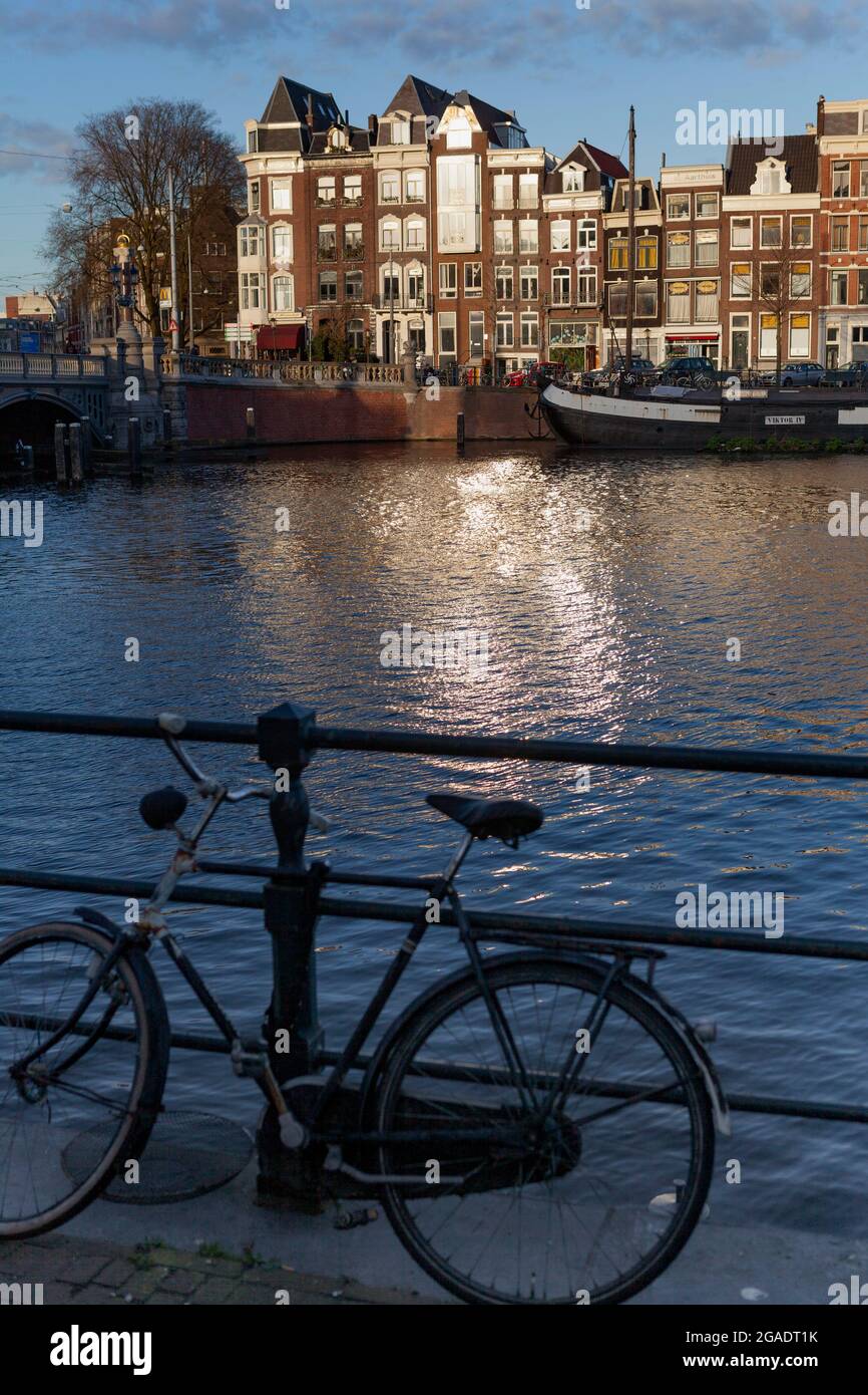 Bicicletta parcheggiata contro la ringhiera dell'Amstel, con il Blauwbrug in lontananza, e il Viktor IV Boathouse, Amsterdam, Paesi Bassi Foto Stock