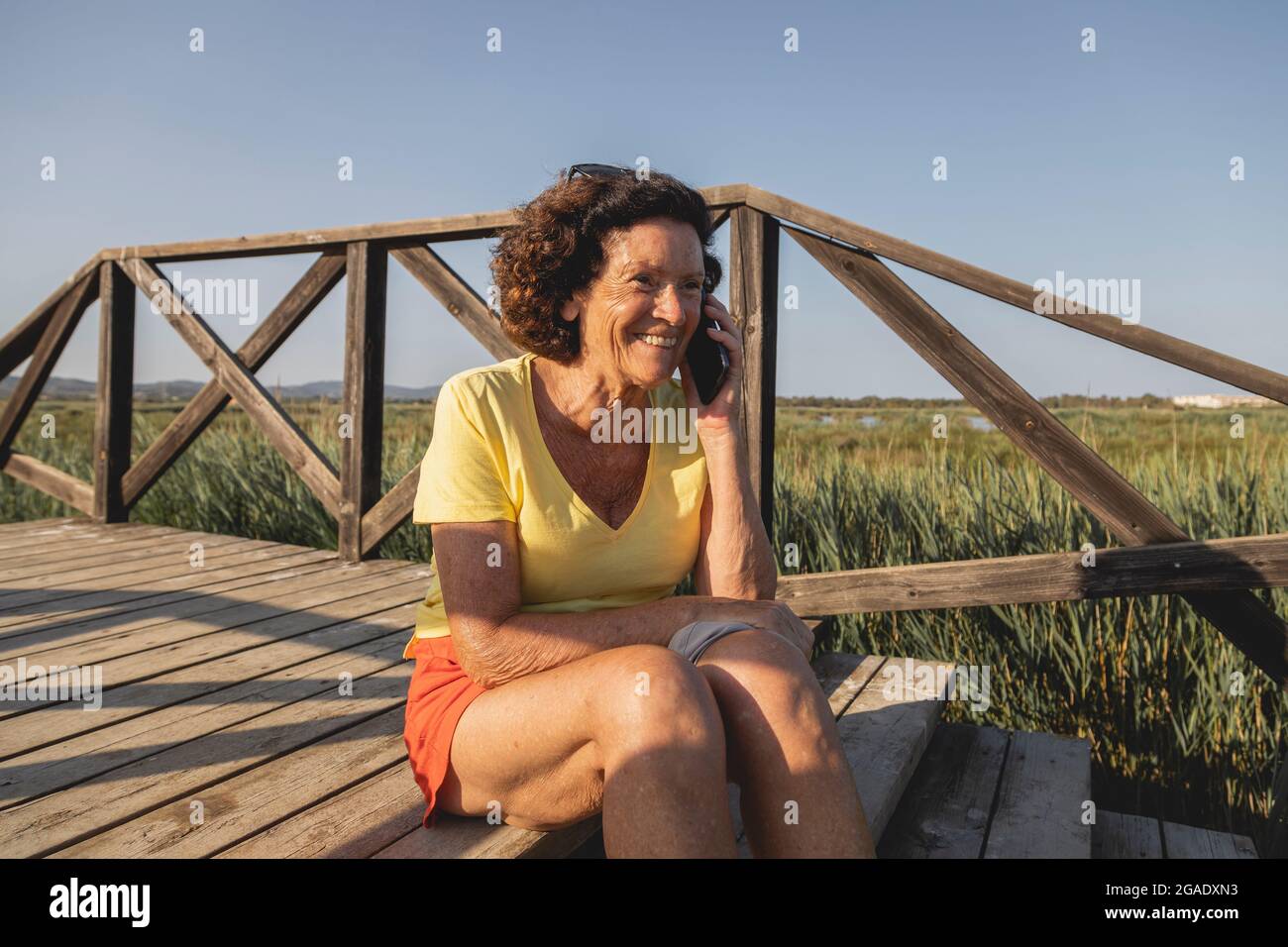Una donna allegra e vitale, negli anni '70, che chiacchiera animatamente al telefono, da una zona naturale vicino al Mar Mediterraneo, in Spagna Foto Stock