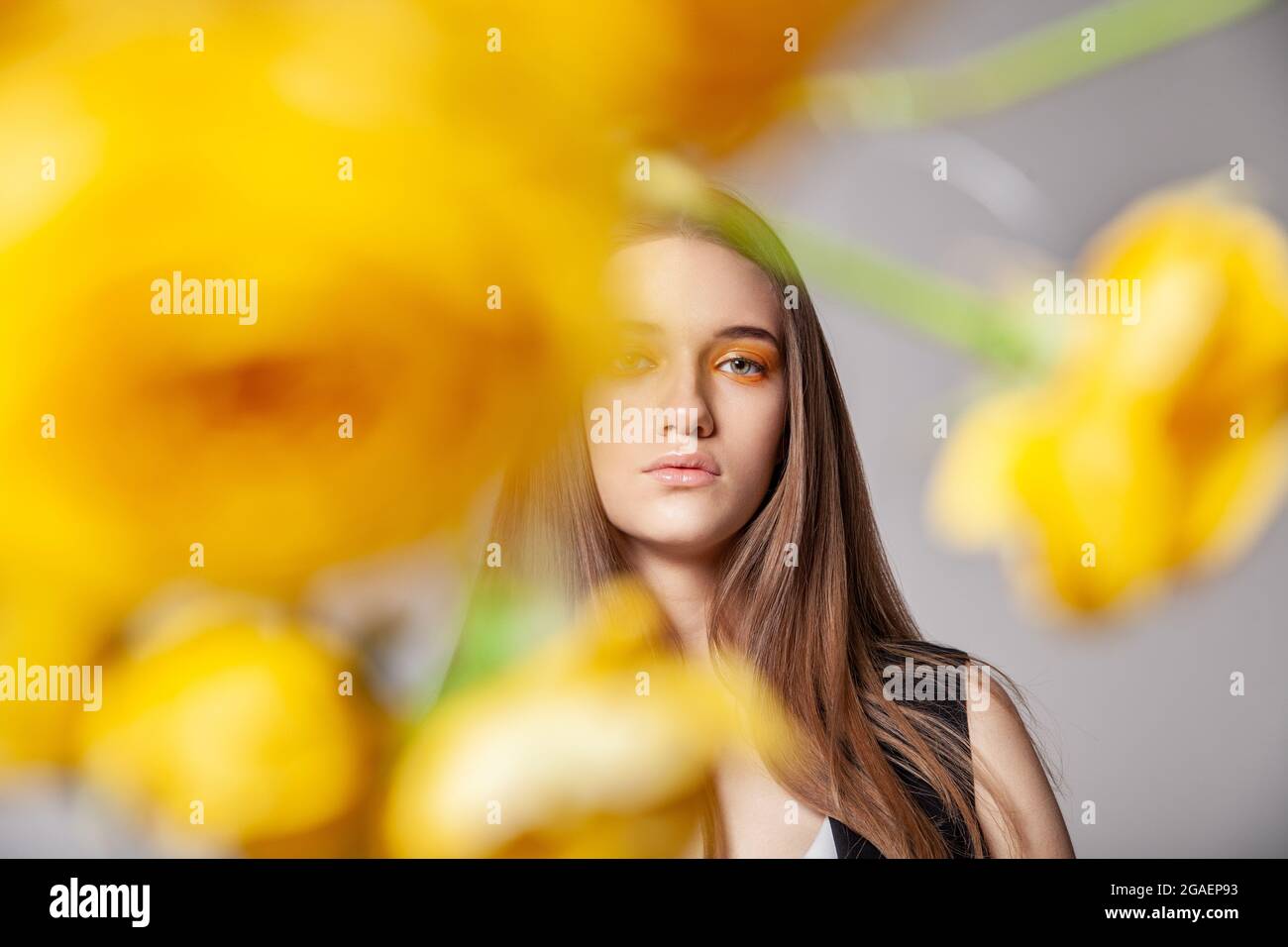 Giovane donna che guarda la macchina fotografica dietro il fiore giallo Foto Stock