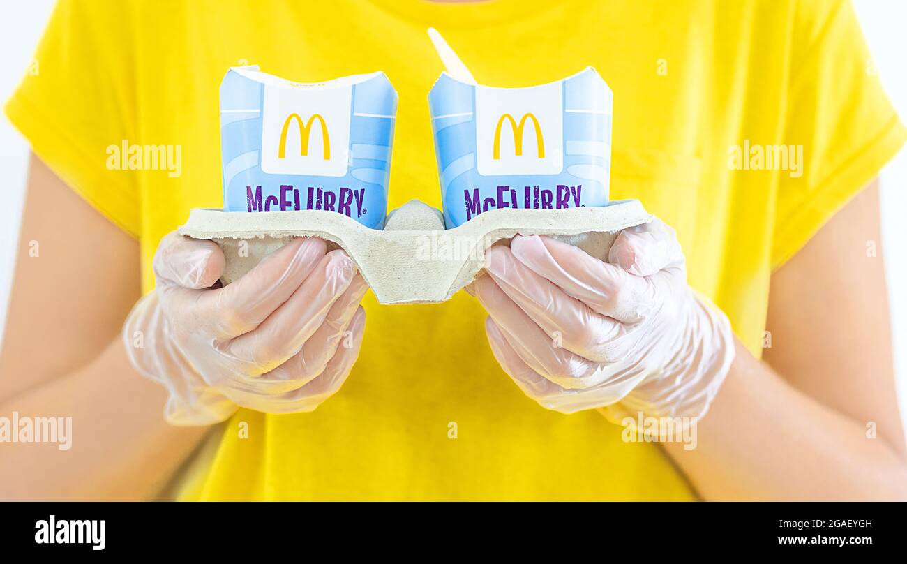Donna in un t-short giallo che tiene un gelato McFlurry in guanti medici. Consegna McCafe. Fast food ristorante McDonalds. Gelateria via Foto Stock